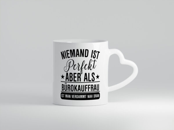 Verdammt nah dran: Bürokauffrau | Kauffrau - Herzhenkel Tasse - Kaffeetasse / Geschenk / Familie