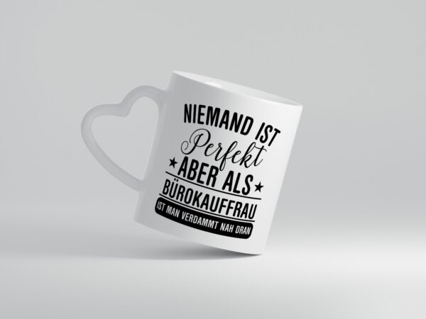 Verdammt nah dran: Bürokauffrau | Kauffrau - Herzhenkel Tasse - Kaffeetasse / Geschenk / Familie